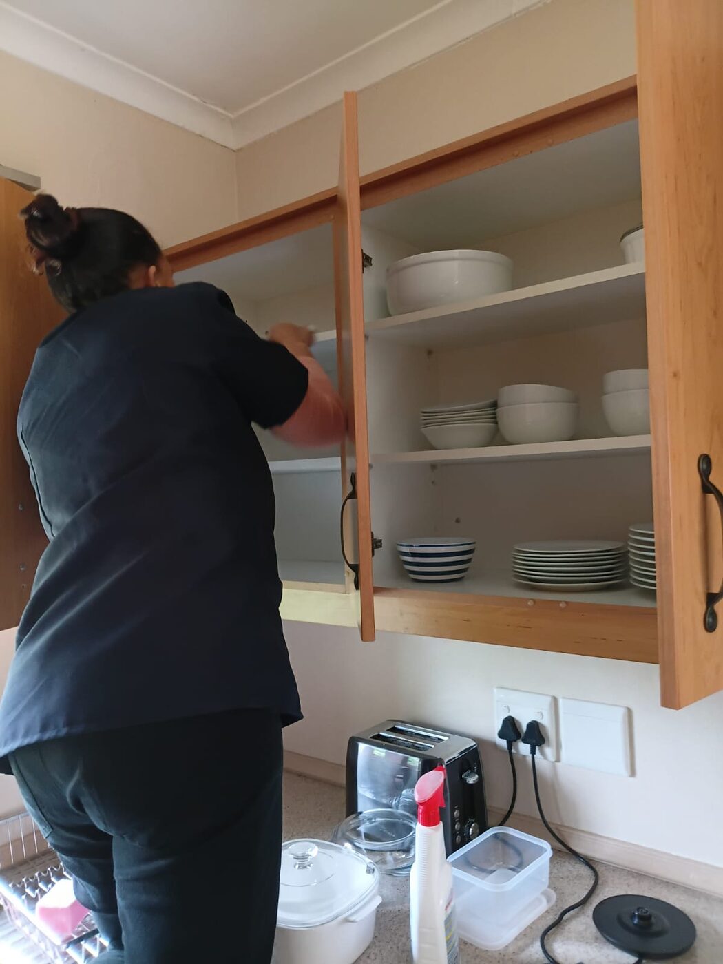 Cayroh team member cleaning inside a kitchen cupboard with the crockery removed