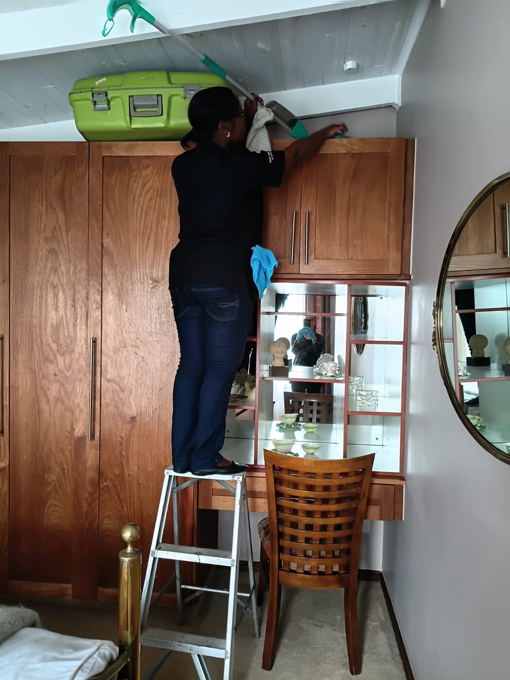 Cayroh team member on a step ladder cleaning the top of a wooden wardrobe