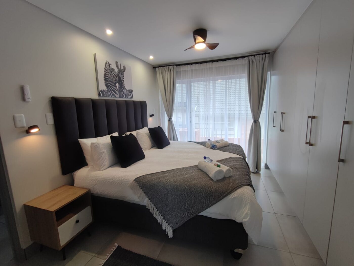 Guest bedroom with an upholstered headboard and rolled towels prepared for check-in by Cayroh